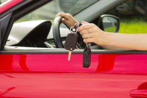 Woman in a red car with keys to a new car
